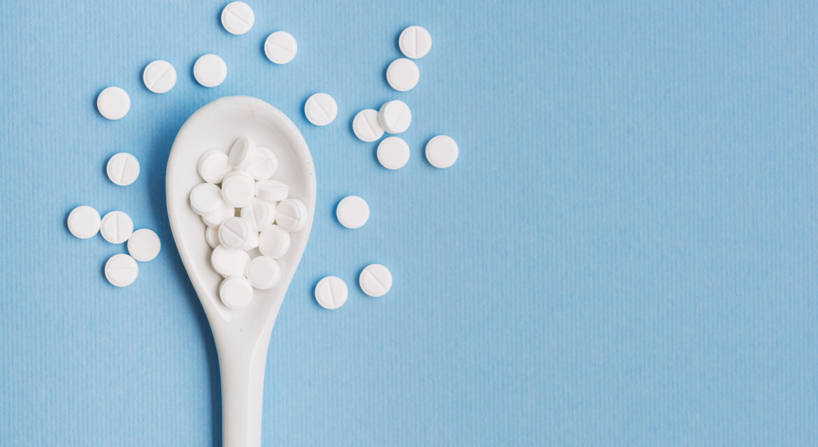White pills on a plastic spoon against a blue background representing male enhancement supplements