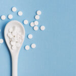 White pills on a plastic spoon against a blue background representing male enhancement supplements